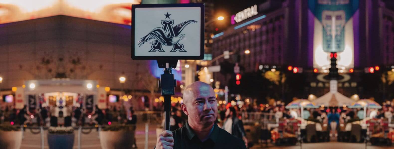 Man holding an illuminated advertising flag in a bustling cityscape at night