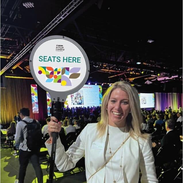 woman holding a sign with seats here caption